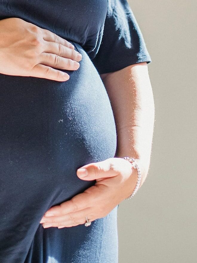 Eine schwangere Frau mit den Händen auf dem Bauch.